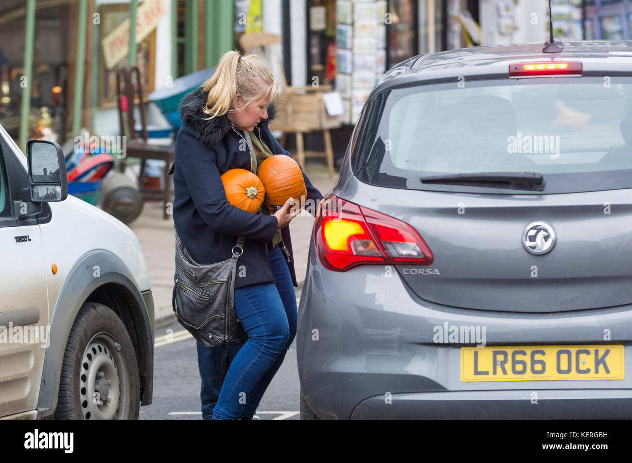 Woman carrying and taking home 2 pumpkins after buying them for Halloween celebrations in the UK. Person with pumpkin. Stock Photo