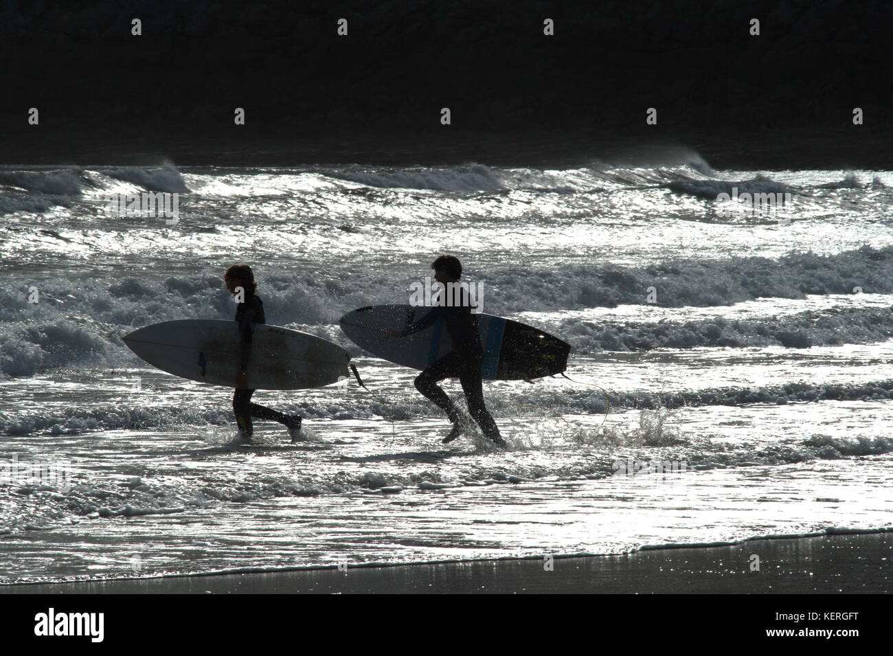 Silhouetted against the sparkling waves two young surfers enter the water together Stock Photo