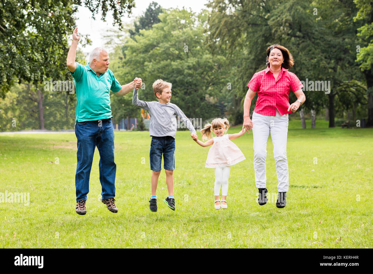 Happy Senior Grandparents Jumping Together With Kids In Park Stock Photo