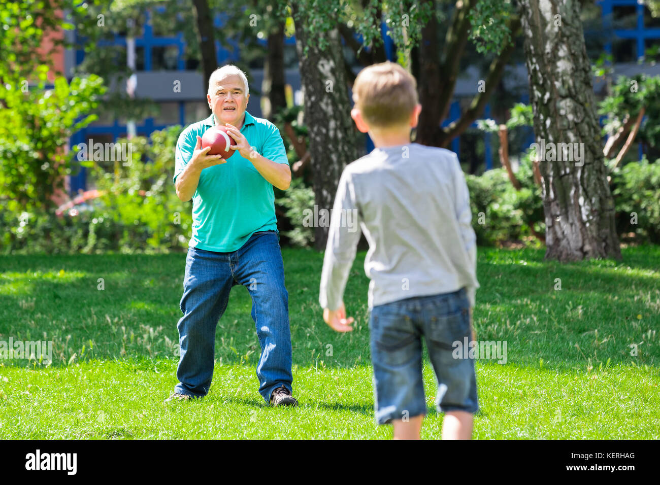 Grandfather Playing American Football Game With Kid In The Park Stock Photo