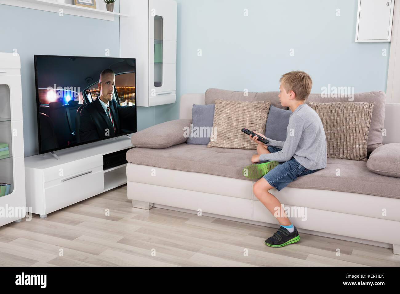 Kid with remote control sitting on couch watching movie on tv Stock Photo