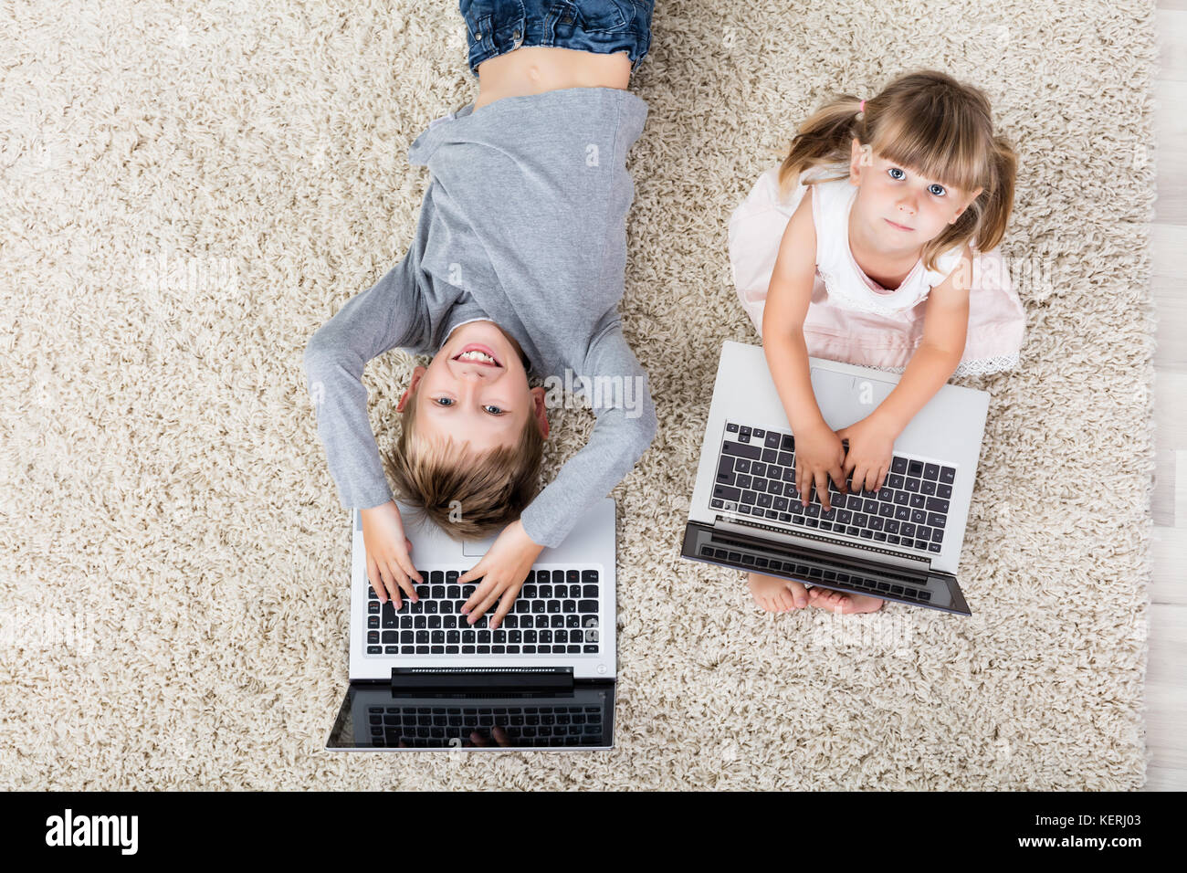 High Angle View Of Kids With Laptop Computer On Carpet At Home Stock Photo