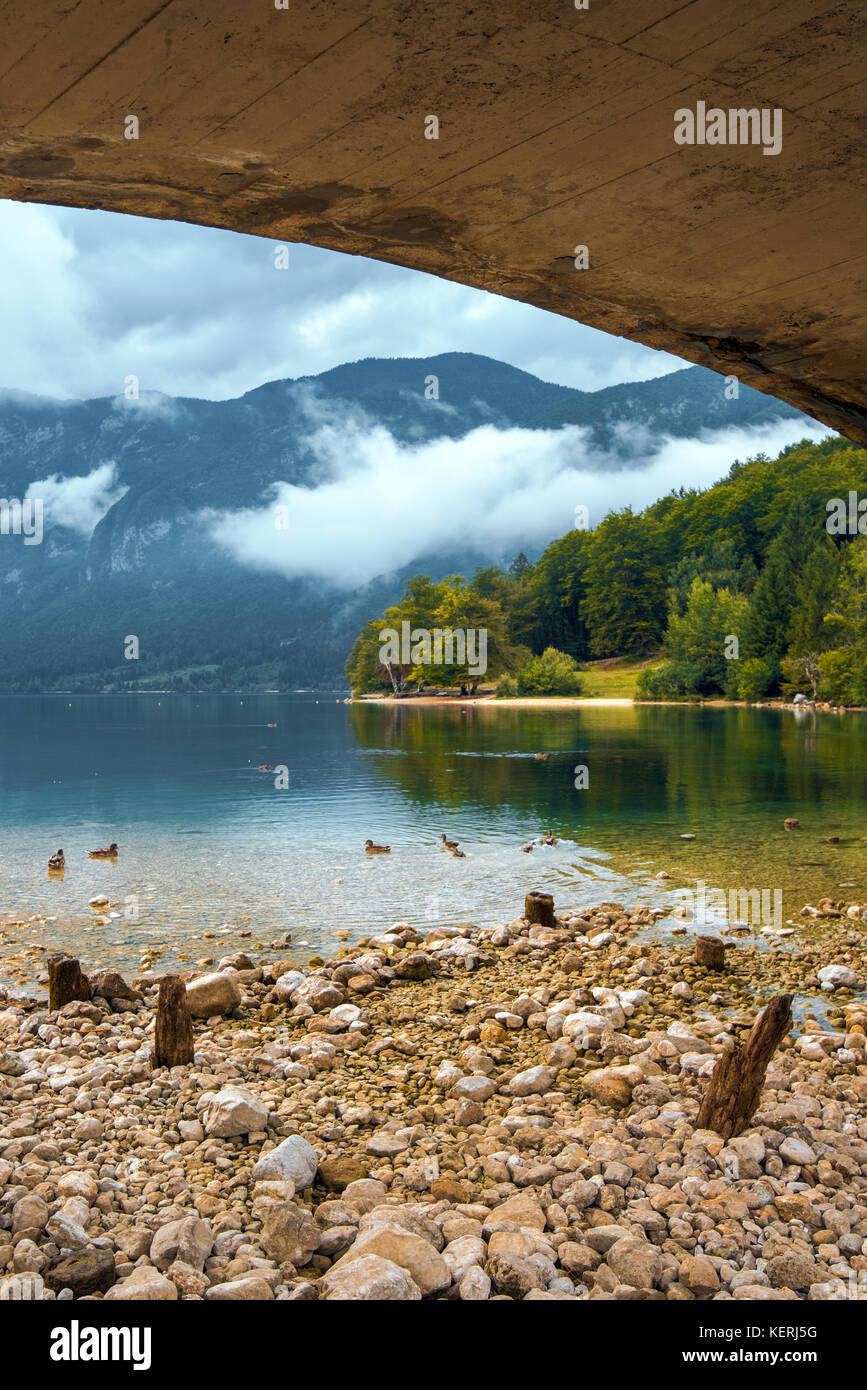 Bohinj lake view from under the bridge. Beautiful glacial lake on a cloudy autumn day. Stock Photo