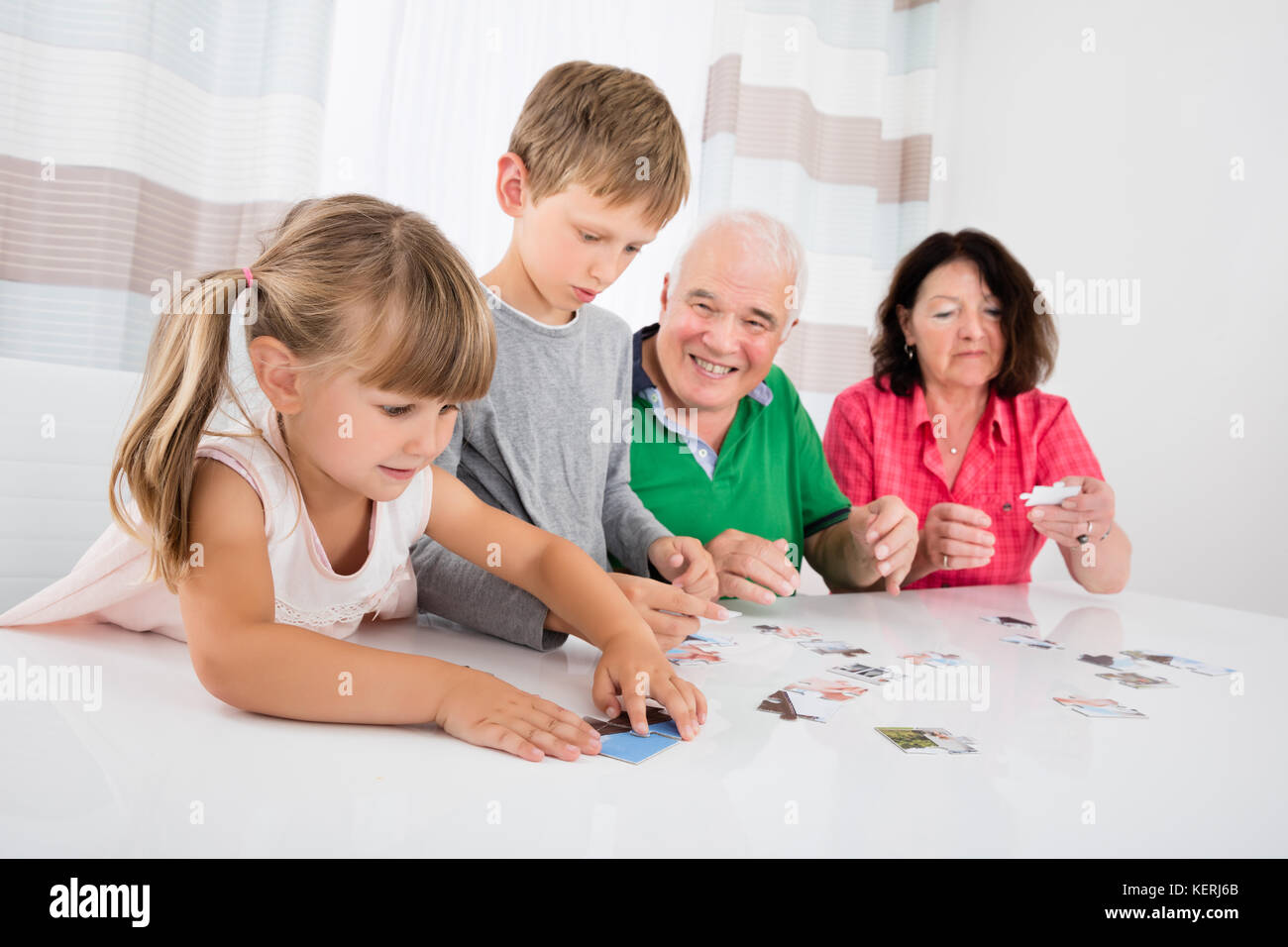 Grandparents Playing Together With Kids Holding Jigsaw Puzzle Pieces At Home Stock Photo