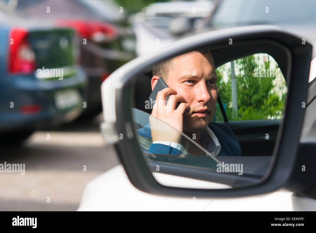 Young man in a jacket talking on the phone, reflection in the mirror of a car Stock Photo