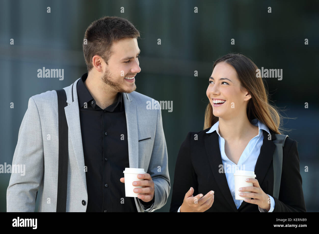 Happy couple of executives walking towards camera and conversing on the street with an office building in the background Stock Photo