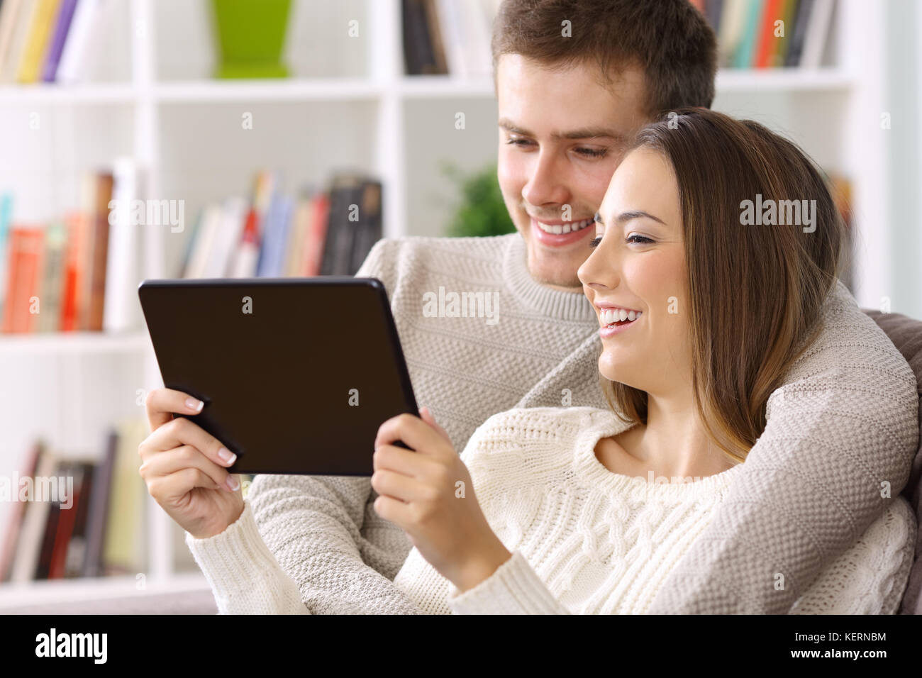 Happy couple watching streaming videos on a tablet sitting on a sofa at home Stock Photo