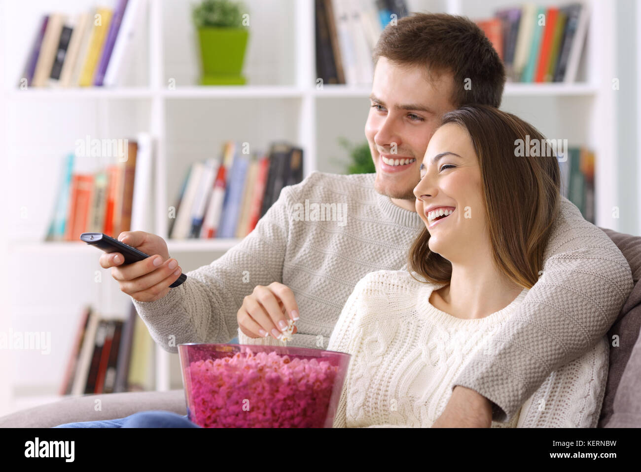 Happy couple watching tv sitting on a couch at home in winter Stock Photo