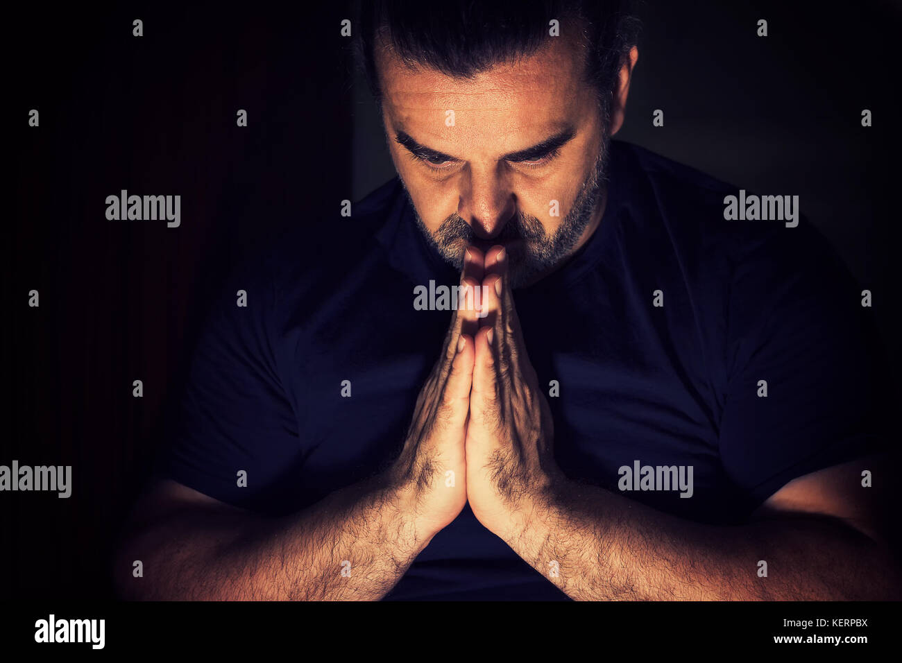 Dark haired man bowing his head in prayer Stock Photo