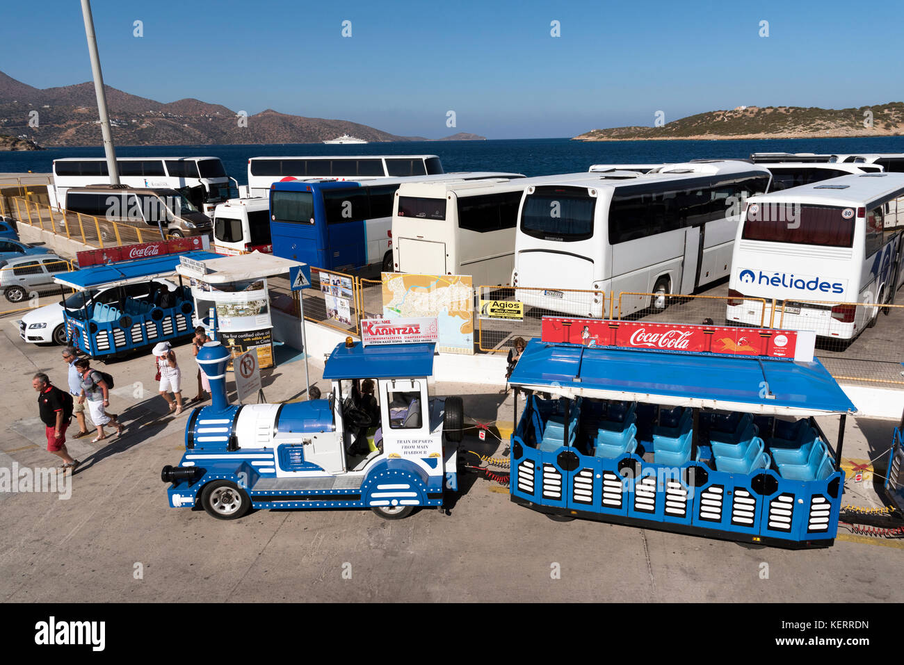 Agios Nikolaos, Crete, Greece. Bus and touist coach park on the harbour frontage. In the foreground a fun tourist little train Stock Photo