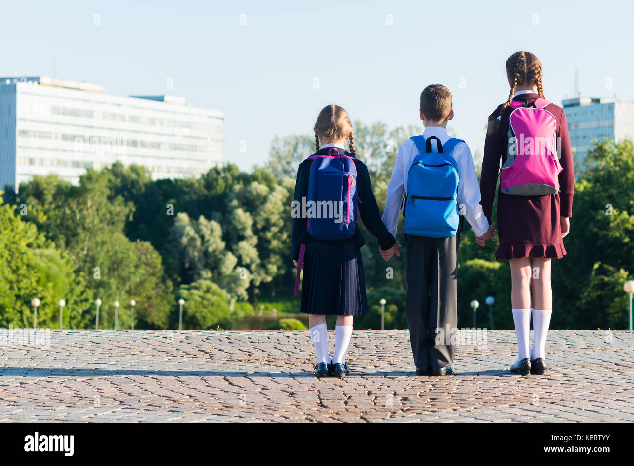 Three pupils in school uniform stand on the street with backpacks, rear view Stock Photo