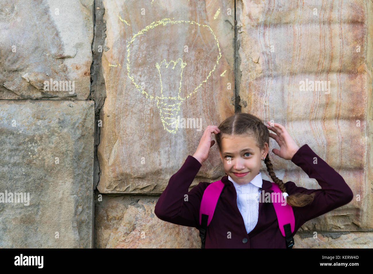girl in school uniform thinks on the background of a stone wall on