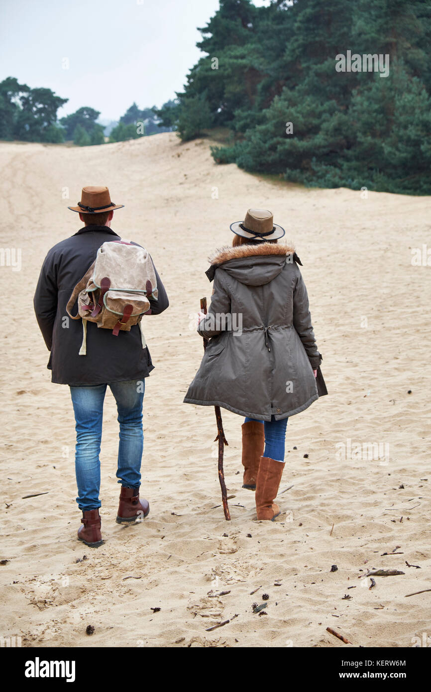 Back view of young couple wearing winter gear hiking across a sand dune area Stock Photo