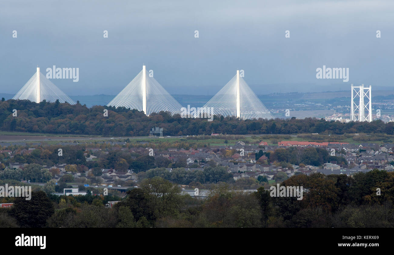 A view of the new Queensferry Crossing and Forth Road Bridge illuminated by the sunshine with Kirkliston village in foreground on a dull October day. Stock Photo
