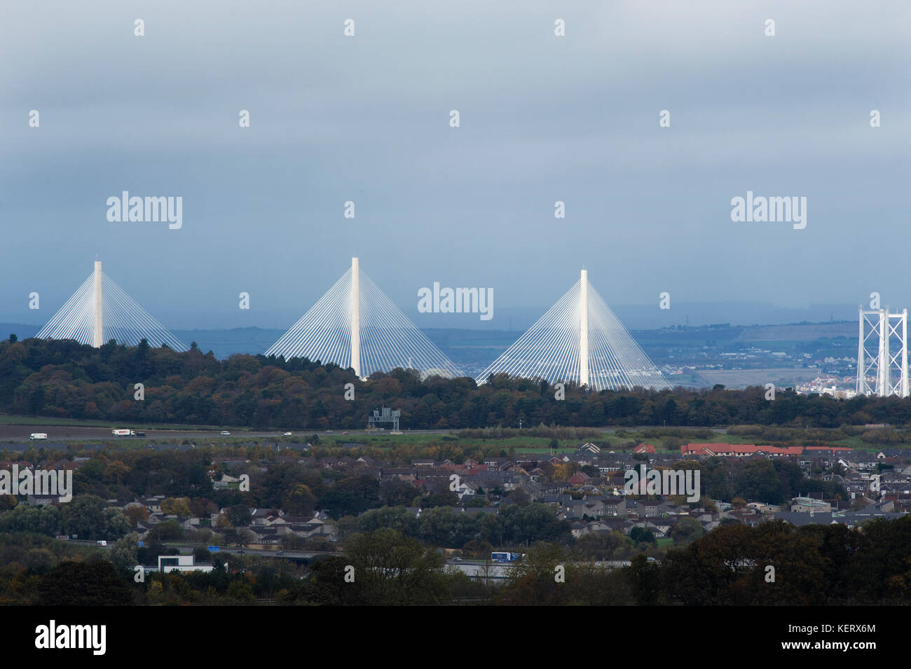 A view of the new Queensferry Crossing and Forth Road Bridge illuminated by the sunshine with Kirkliston village in foreground on a dull October day. Stock Photo