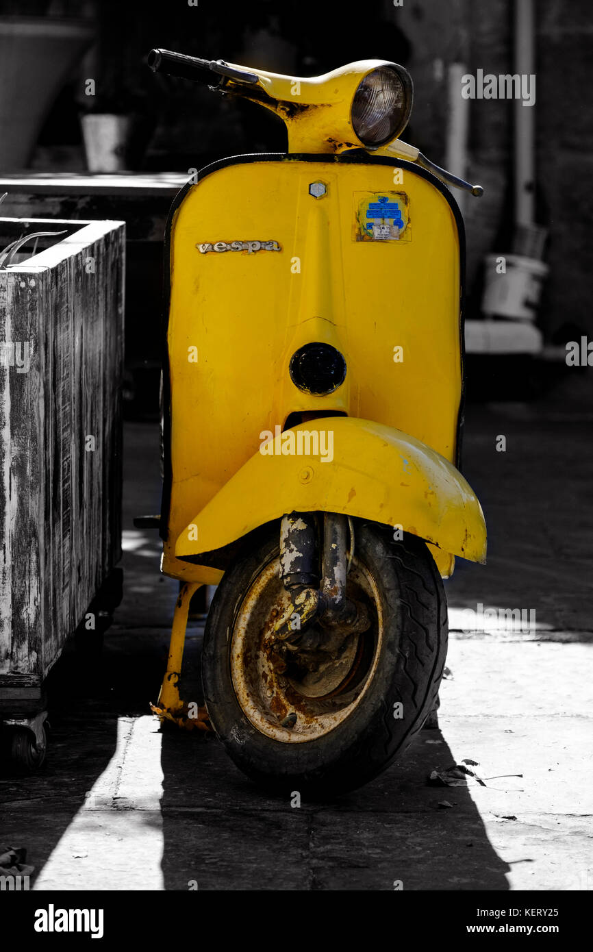 An old, hand painted, yellow vespa scooter parked up and unattended on the pavement Stock Photo