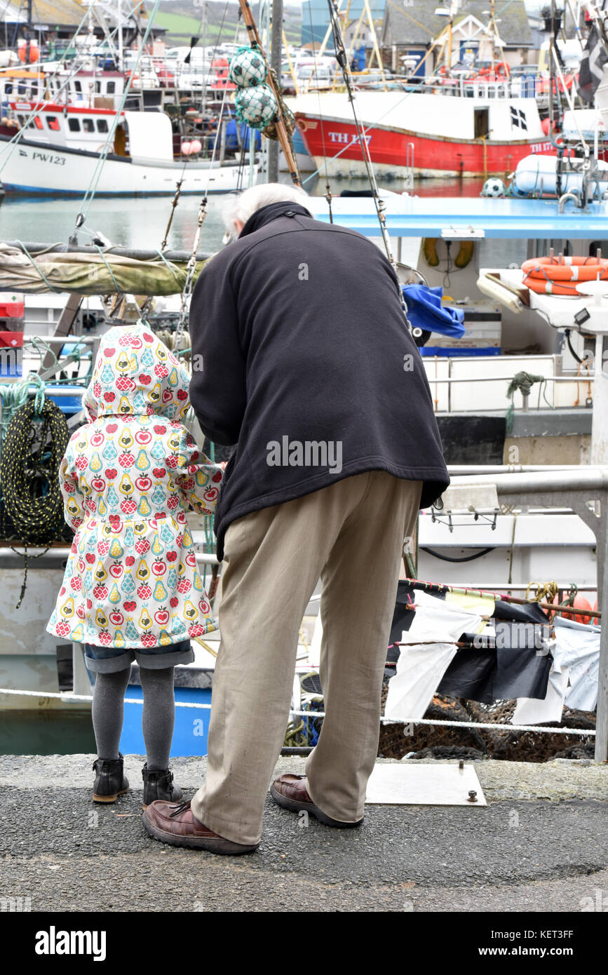 A young child or girl in a spotty raincoat being taught or shown how to fish and catching crabs with or by her grandad or grandfather in padstow. Stock Photo