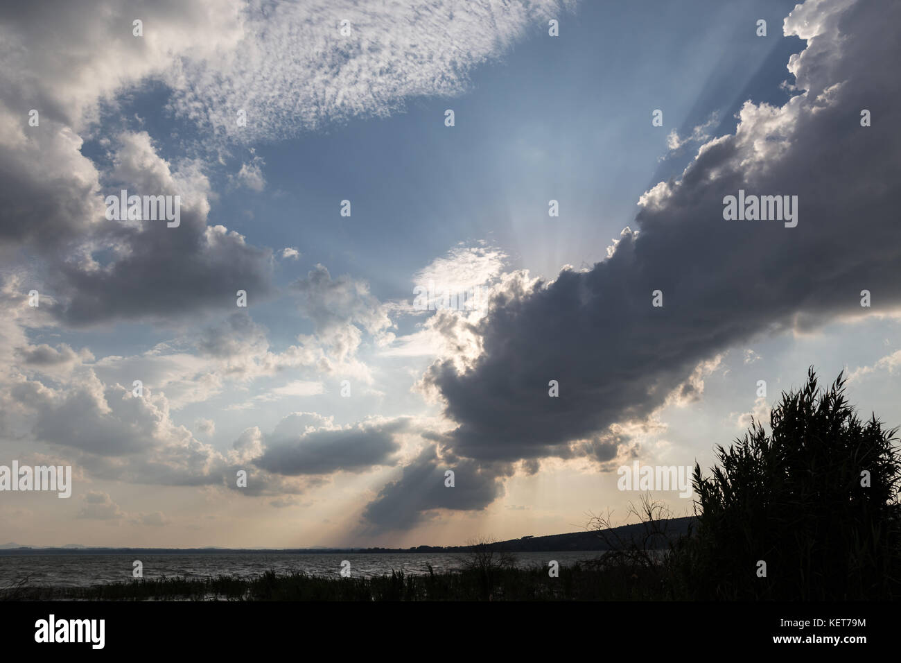 Powerful sun rays coming out through some clouds above a lake shore Stock Photo