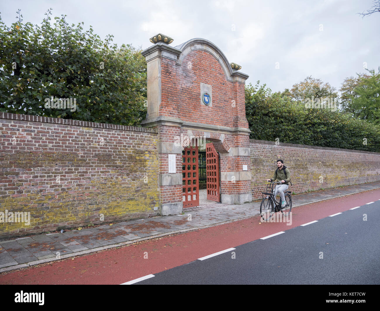 young man on bicycle passes old wall and entrance to prinsentuin in dutch town of groningen Stock Photo