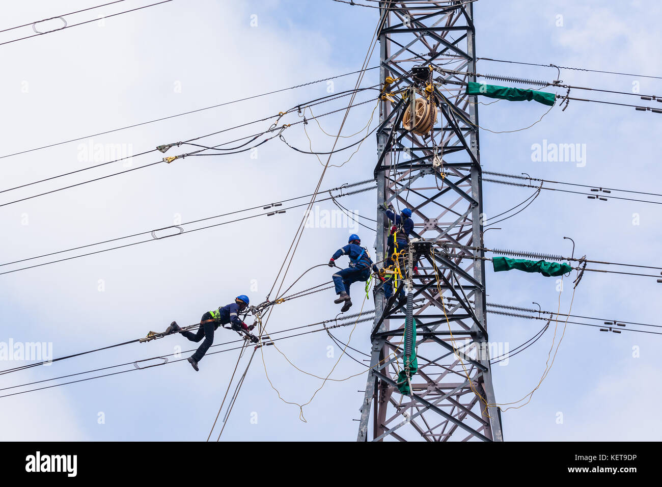 Electricians hanging on steel cables high above ground working on