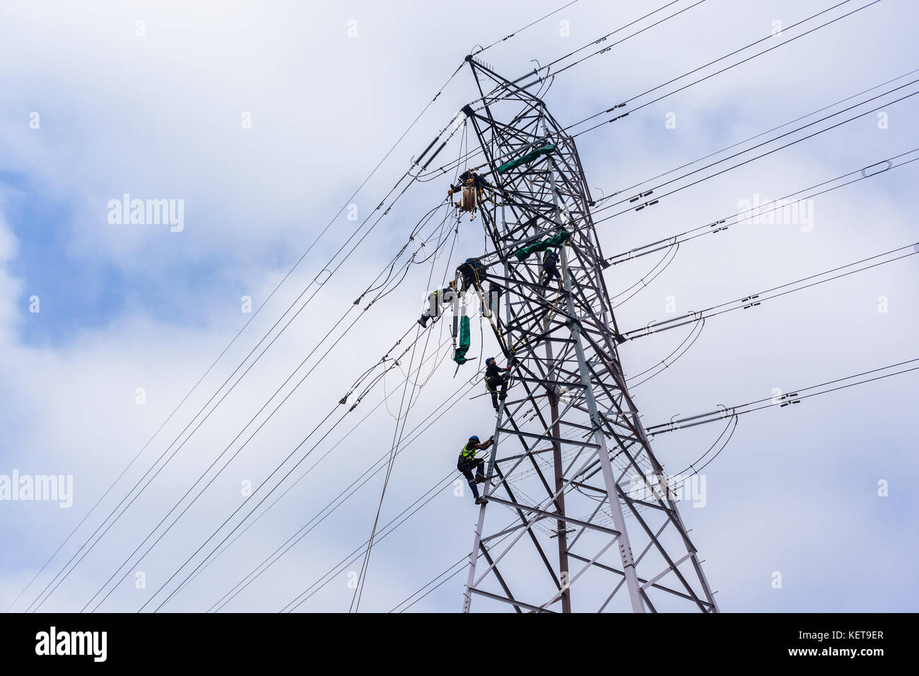 Electricians working on electrical cable power lines on steel tower. Stock Photo