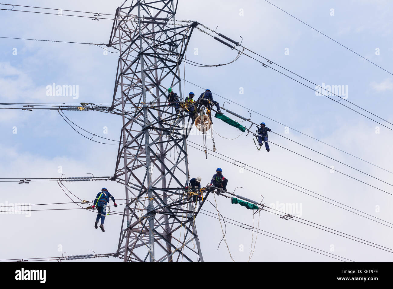 Electricians working on electrical cable power lines on steel tower. Stock Photo