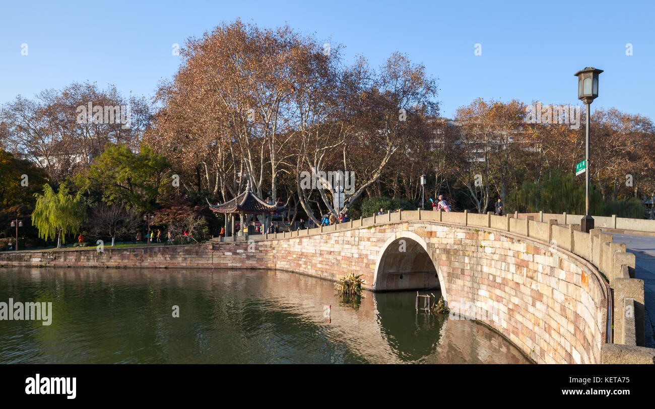 Hangzhou, China - December 5, 2014: West Lake, famous park in Hangzhou city. Ordinary people walk on stone bridge Stock Photo