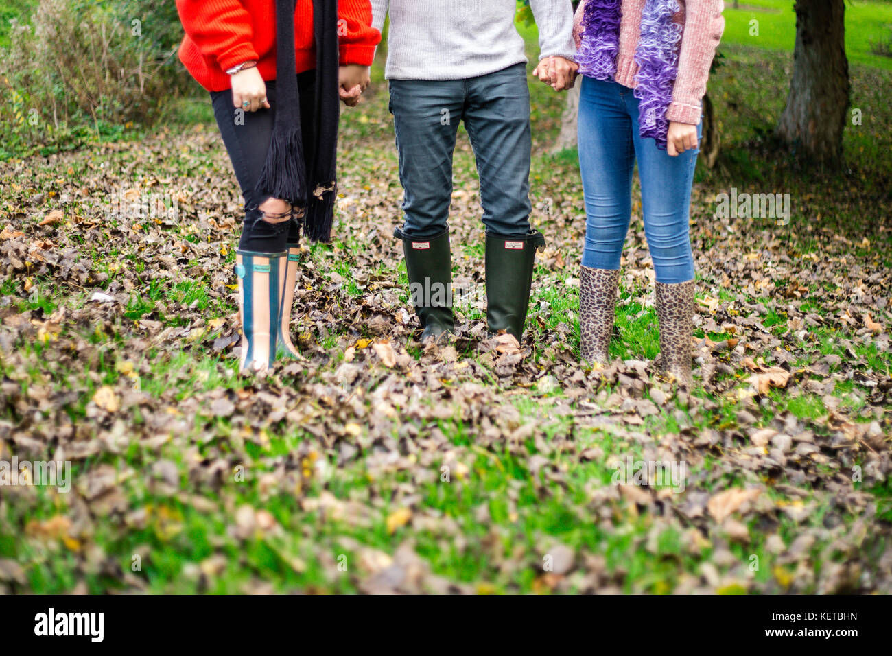 three people kicking leaves in woodland / park Stock Photo