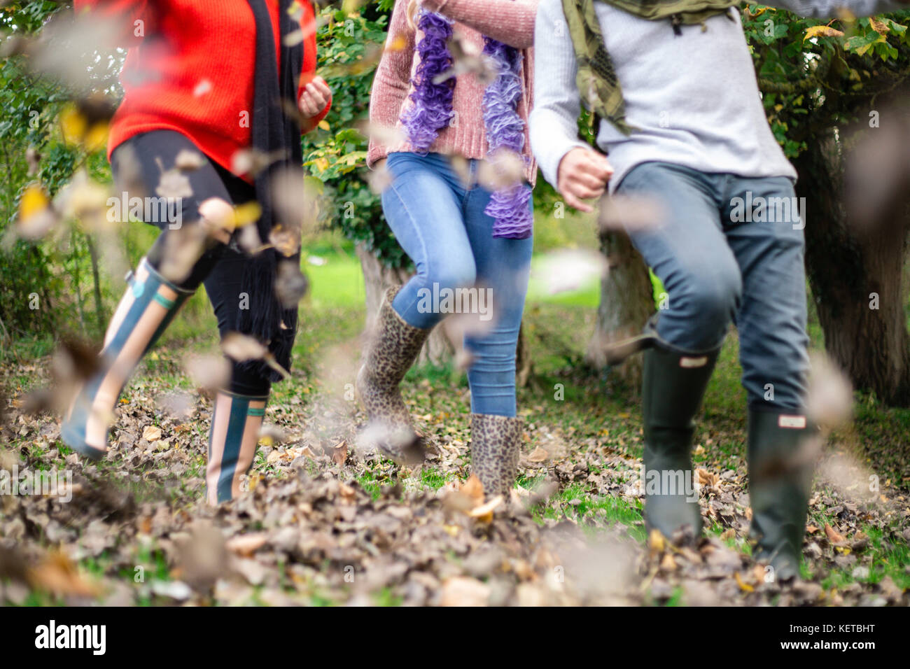 three people kicking leaves in woodland / park Stock Photo