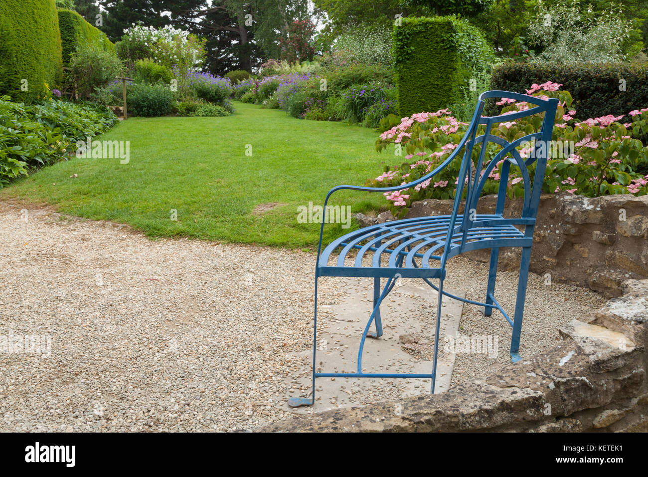 A stylishly shaped wrought-iron seat looks towards the Wide border of Kiftsgate Court near Chipping Campden, Cotswolds, Gloucestershire, England. Stock Photo