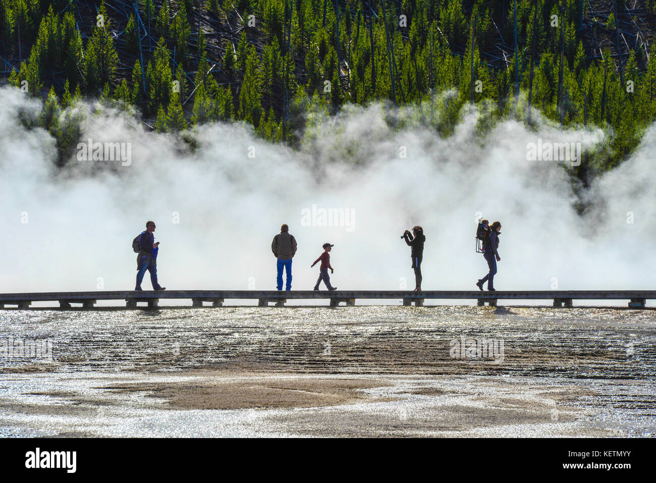 YELLOWSTONE, MONTANA USA. Tourists crossing the Grand Prismatic Spring in Yellowstone Nationalpark on a boardwalk surrounded by vapor. This geyser is  Stock Photo