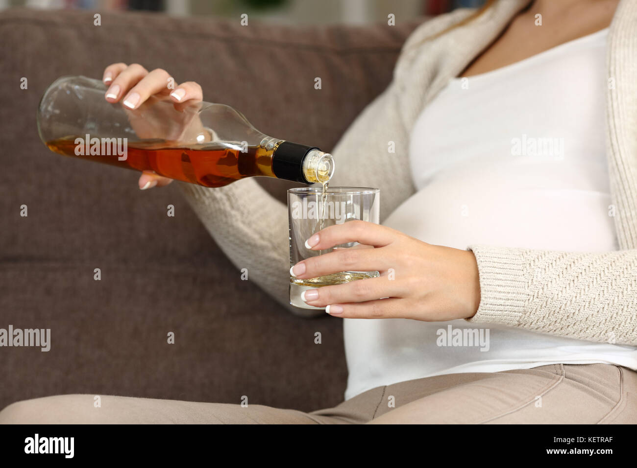 Close up of an irresponsible pregnant woman drinking alcohol sitting on a couch at home Stock Photo