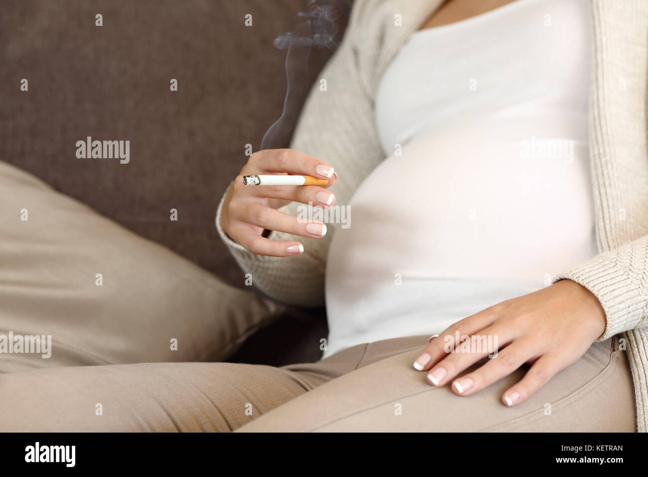Close up of an irresponsible pregnant woman smoking a cigar sitting on a sofa at home Stock Photo