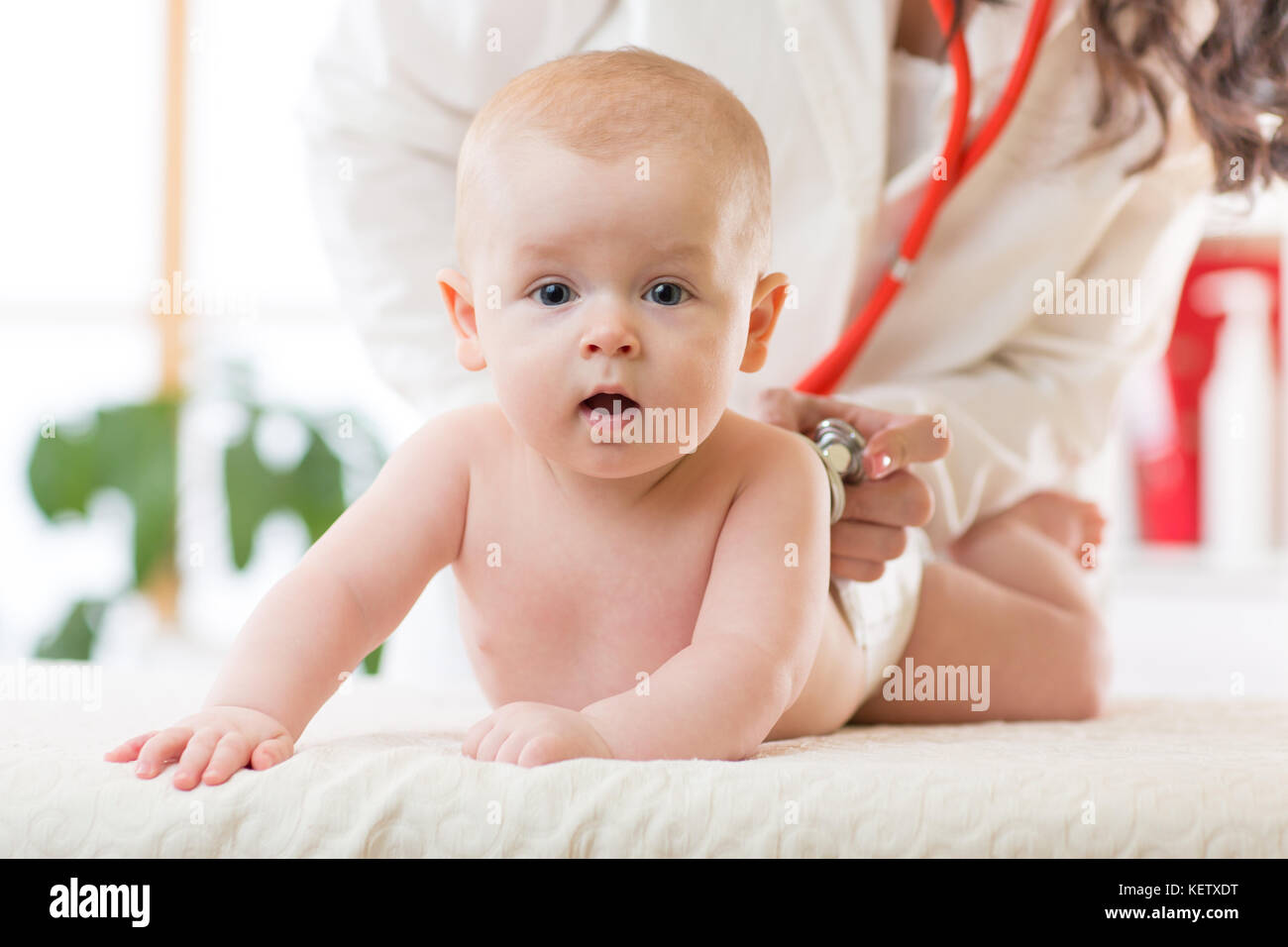 Pediatrician examines newborn baby boy. Doctor using a stethoscope to listen to child's back checking heart beat. Kid is looking at camera. Stock Photo