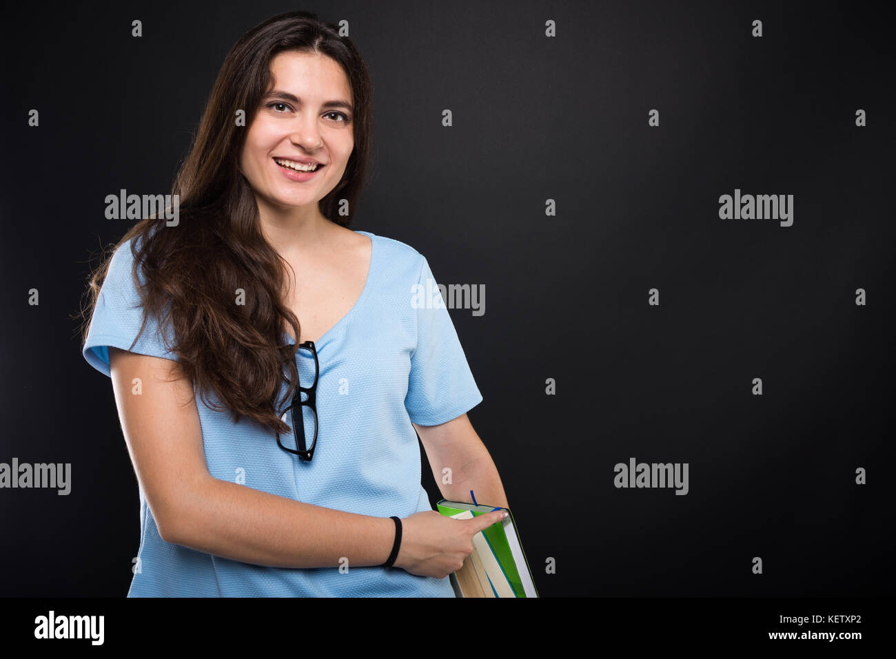 Beautiful teenage girl holding a pile of books and pointing to them on ...