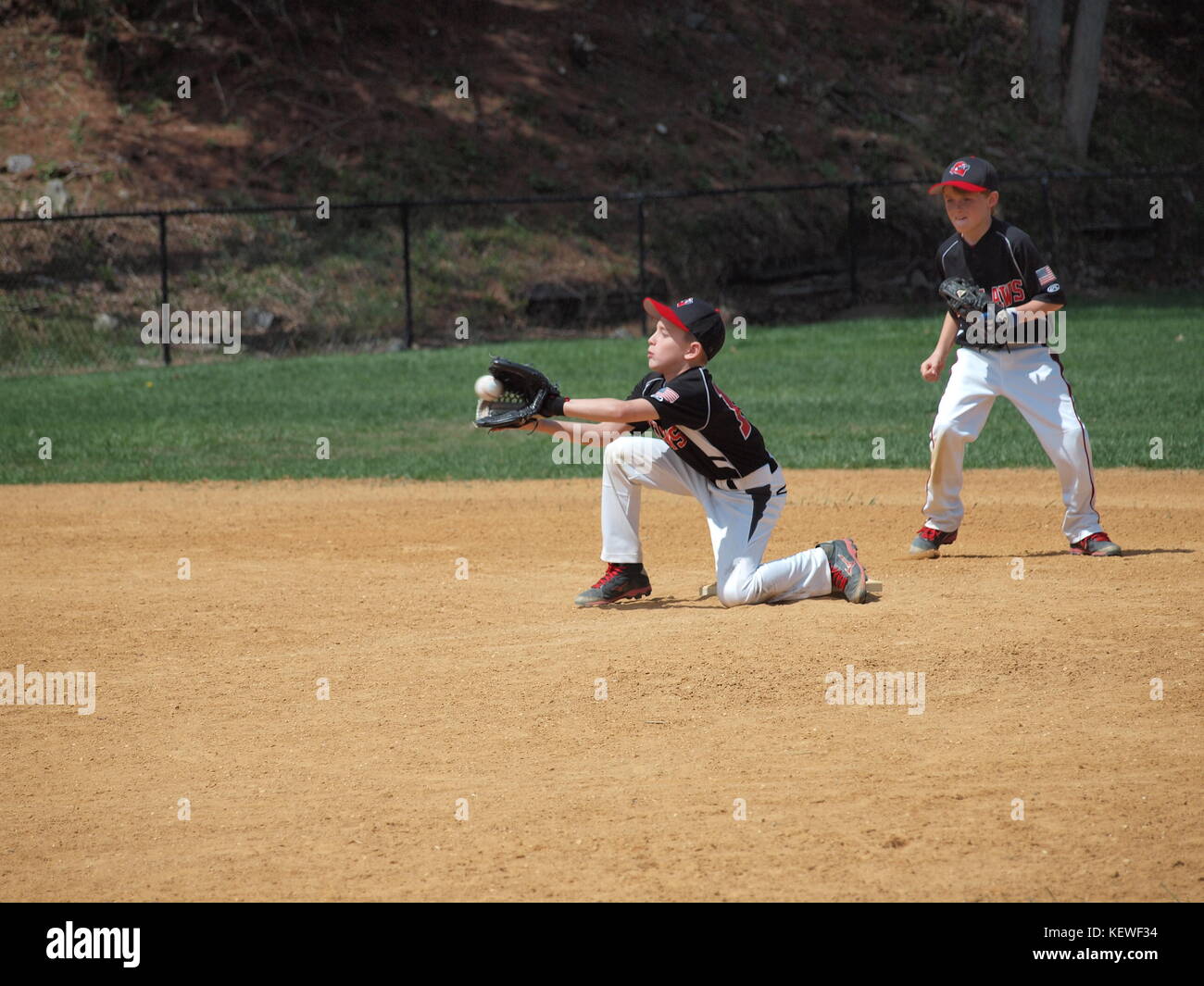 Little League fielder stopping ball during hot summer day. Stock Photo