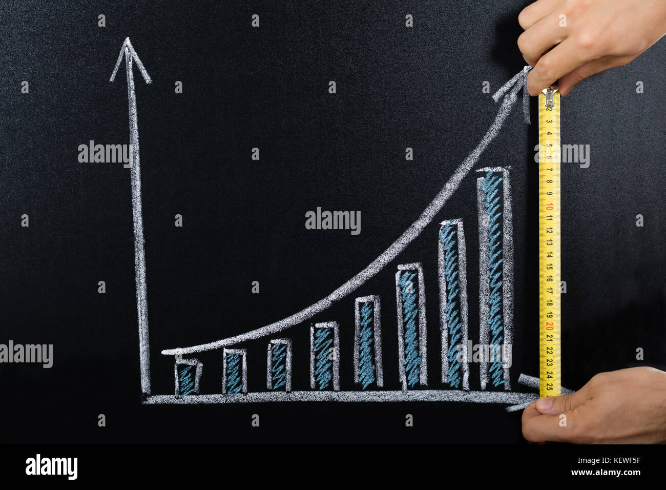 Close-up Of A Person Measuring Business Graph On Blackboard Using Scale Stock Photo