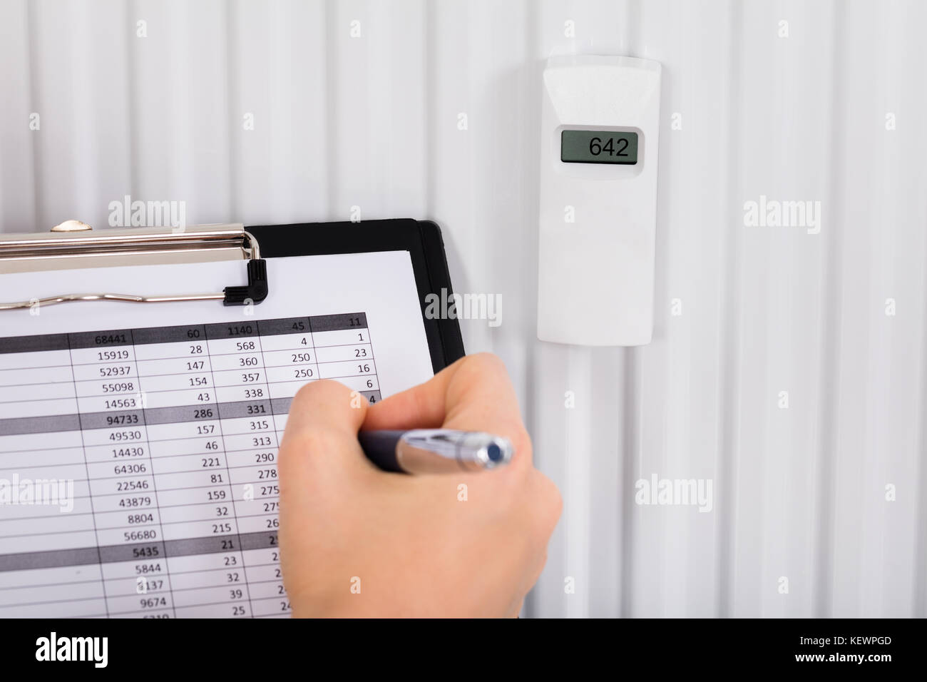 Person Hand Maintaining Records Of Digital Thermostat On Clipboard At Home Stock Photo