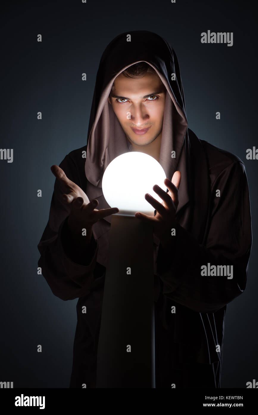 Young wizard with crystal ball in dark room Stock Photo