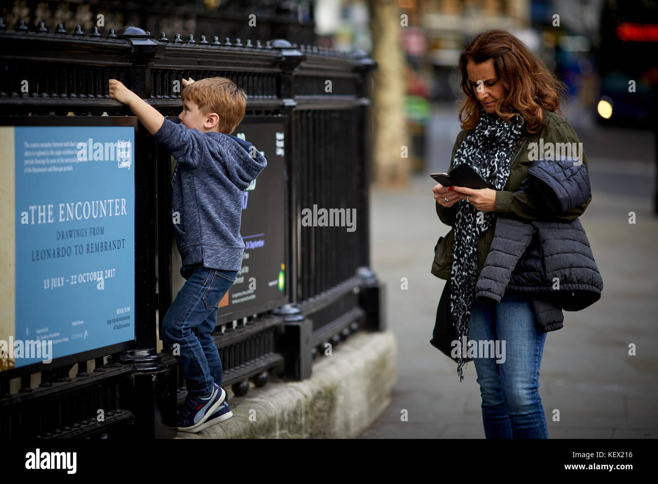 Mum texting as child plays on railings National Portrait Gallery in London the capital city of England Stock Photo