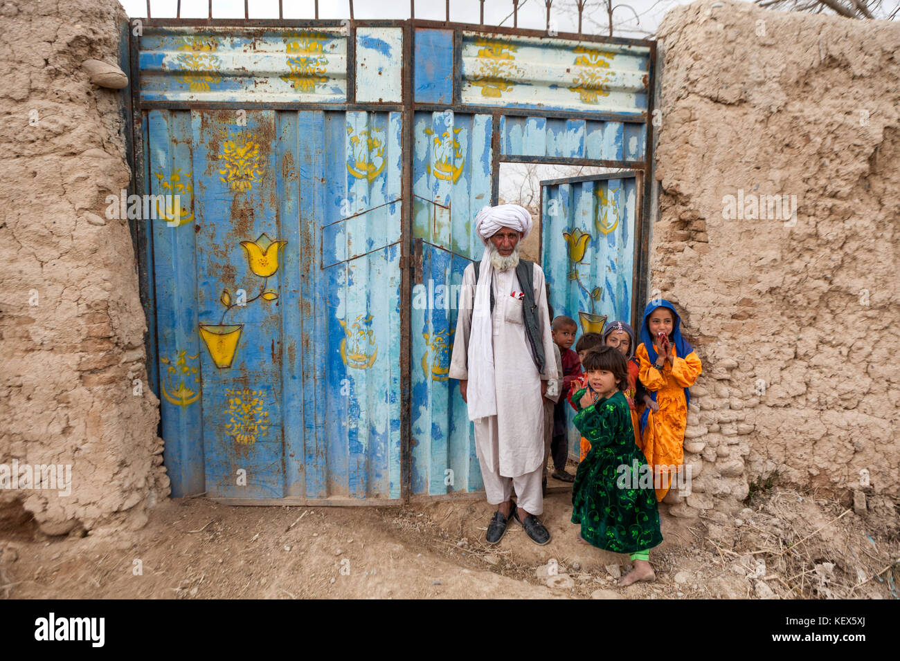 An Afghan man stands outside the gate to his compound with young ...
