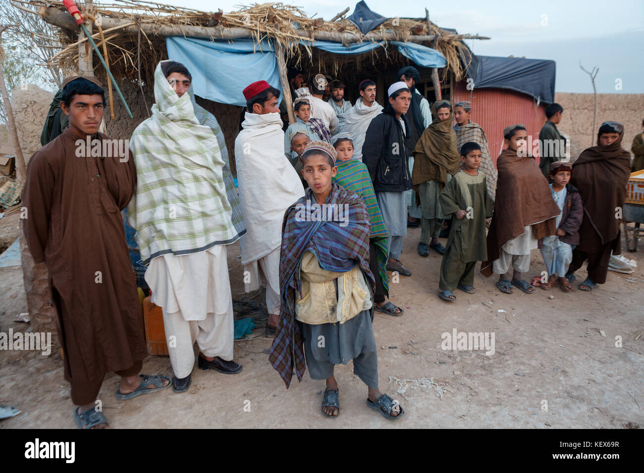 Afghan Men and Boys stan outside a stall on a dusty street in Helmand Province, Afghanistan Stock Photo