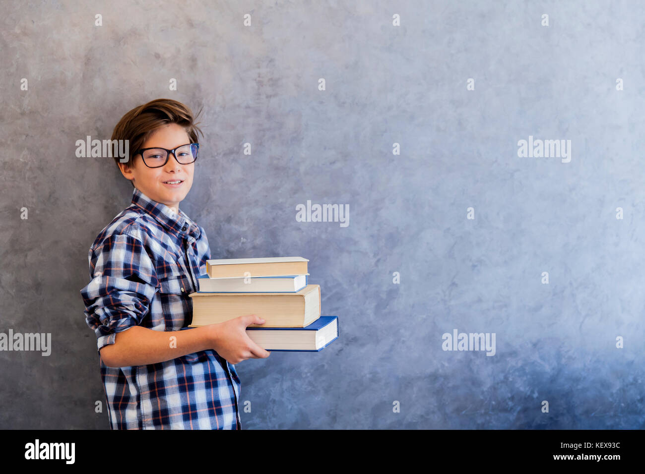 Cute teenage school boy holding books against wall Stock Photo - Alamy