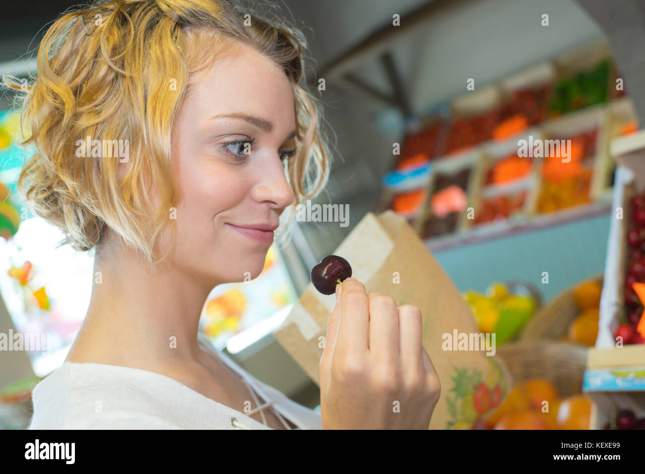 attractive young grocery clerk tasting cherry in grocery store Stock