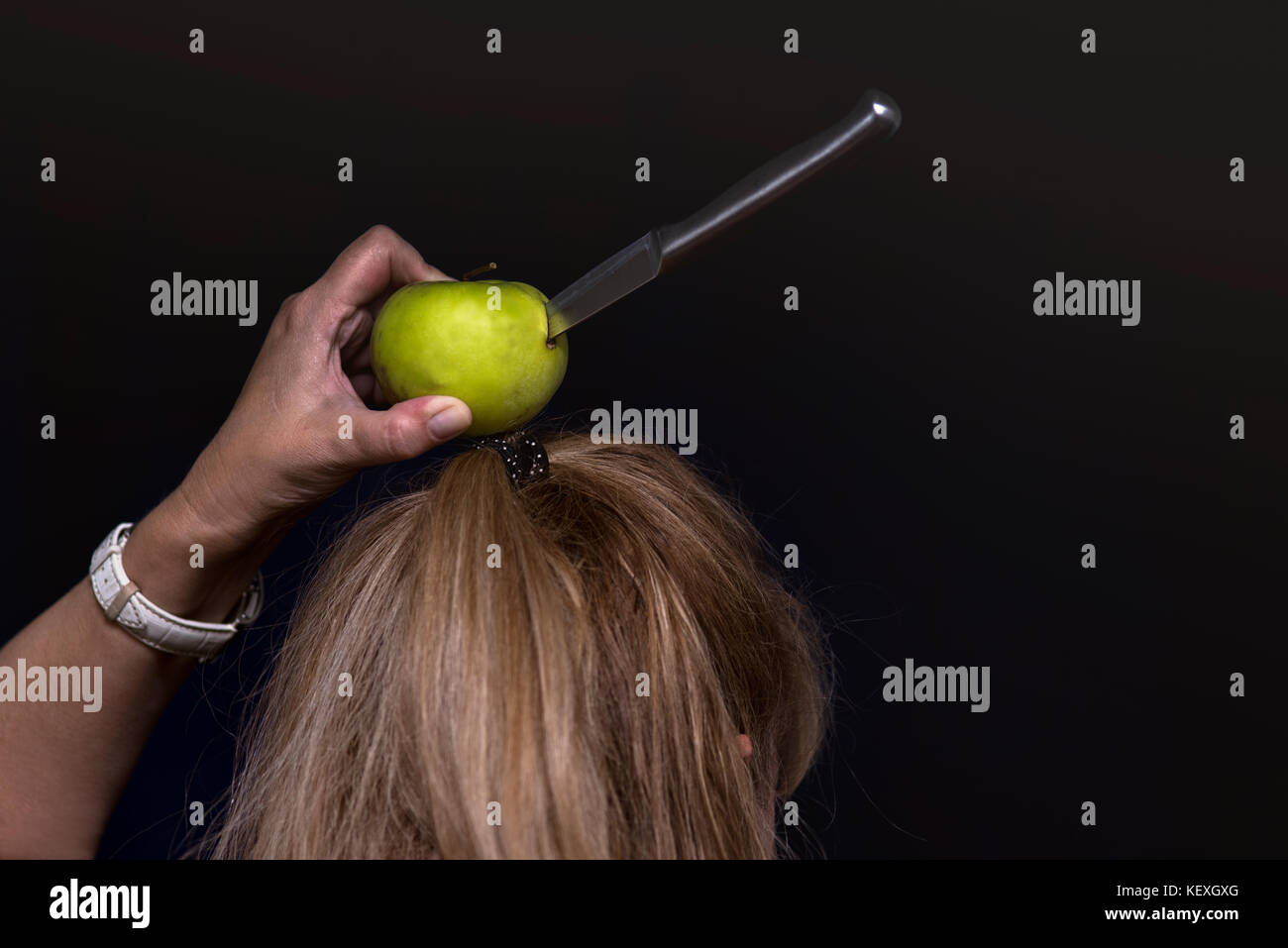 Brave woman playing a role of a human target with apple and knife on her head Stock Photo