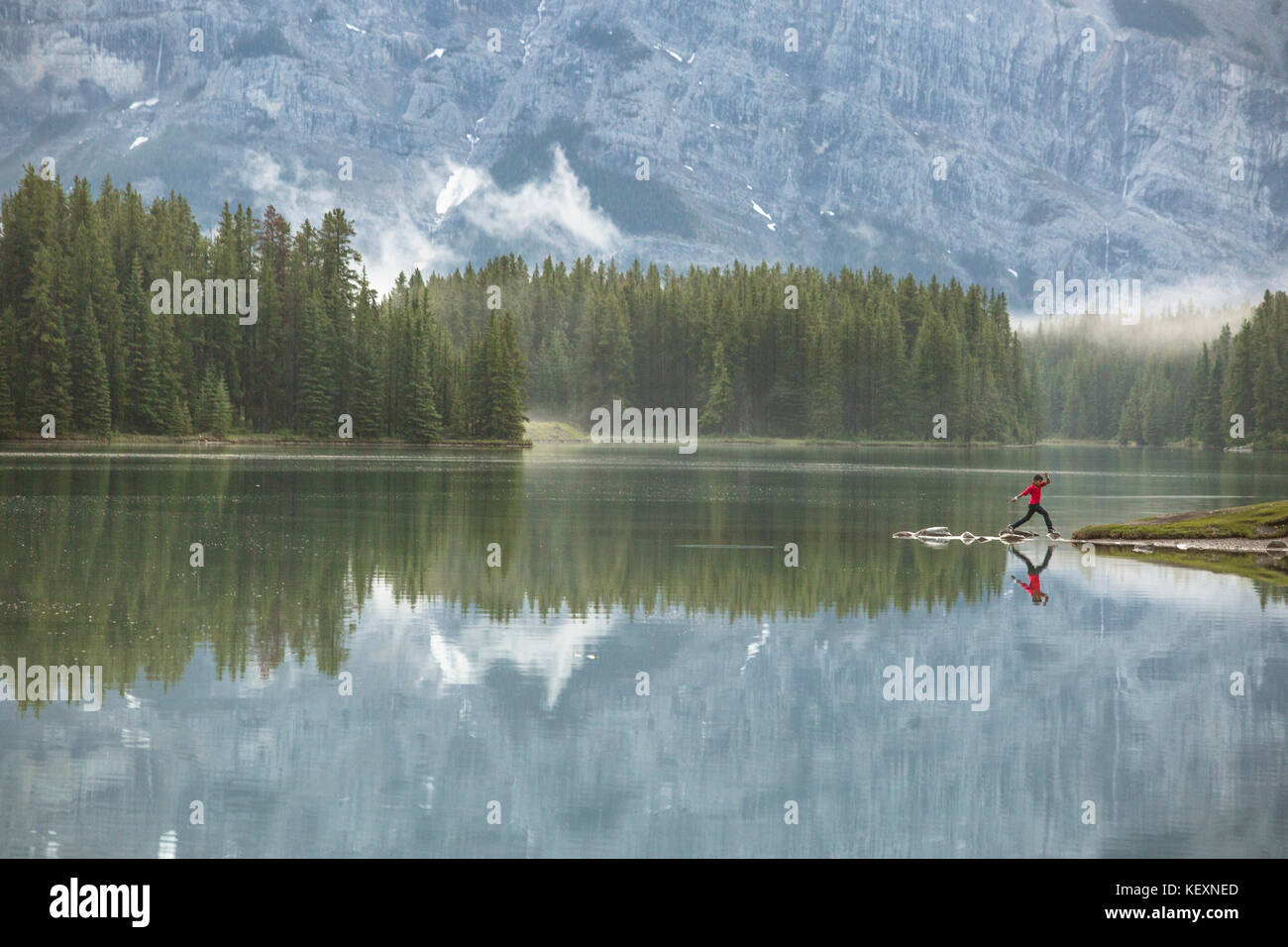 Majestic natural scenery with boy jumping from rock to rock to get to shore of Two Jack Lake, Banff National Park, Alberta, Canada Stock Photo