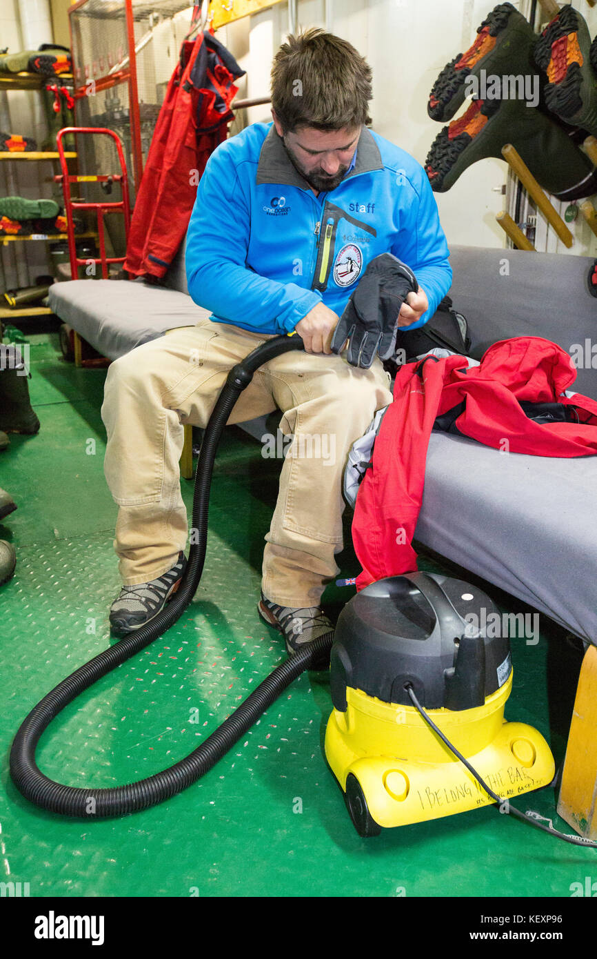 Man sitting inside ship cabin vacuuming clothes, Antarctica Stock Photo