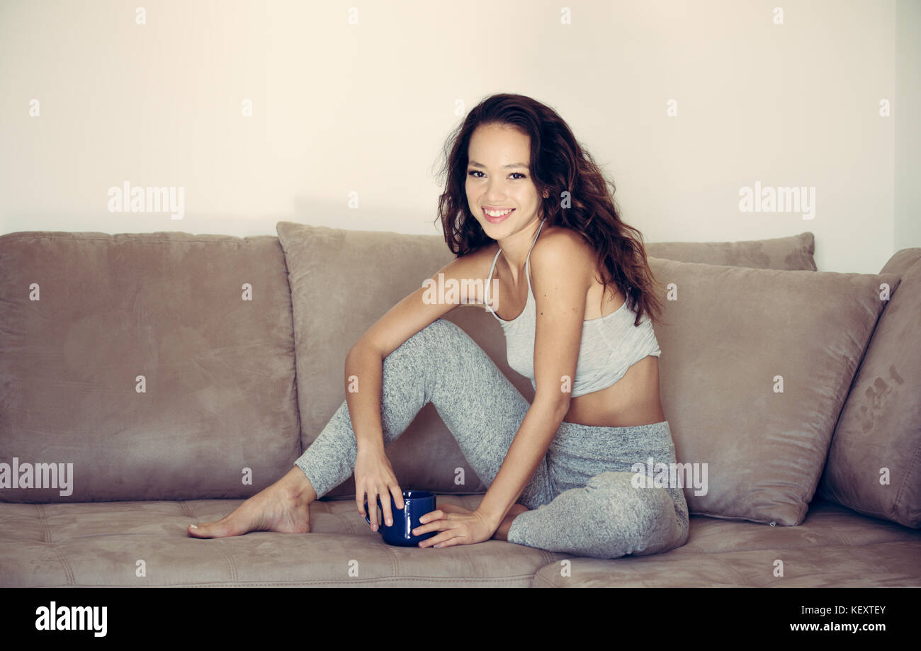 Young pretty asian woman sitting on the couch relaxed smiling face expression looking at camera blue mug in the hands Stock Photo