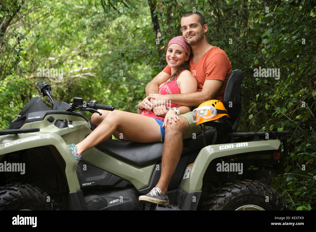Couple smiling and embracing while sitting on quad bike in Emotions Native Park, Quintana Roo, Mexico Stock Photo