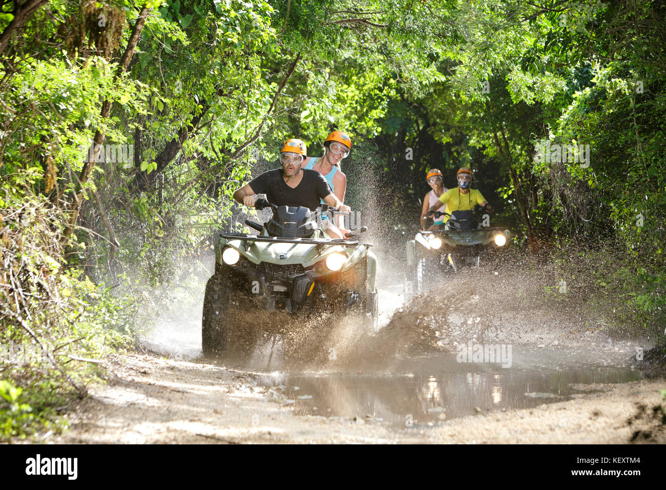 Front view of couples driving quad bikes through dirt road puddles in Emotions Native Park, Quintana Roo, Mexico Stock Photo
